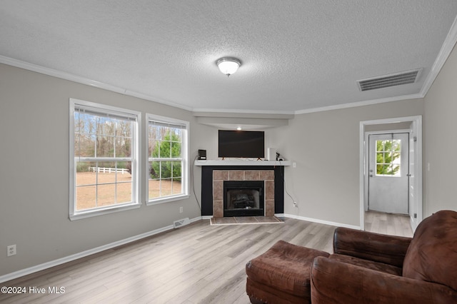 living room with a textured ceiling, light hardwood / wood-style flooring, crown molding, and a tiled fireplace