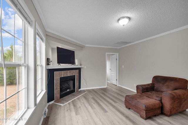 living area with light hardwood / wood-style floors, ornamental molding, a textured ceiling, and a tile fireplace