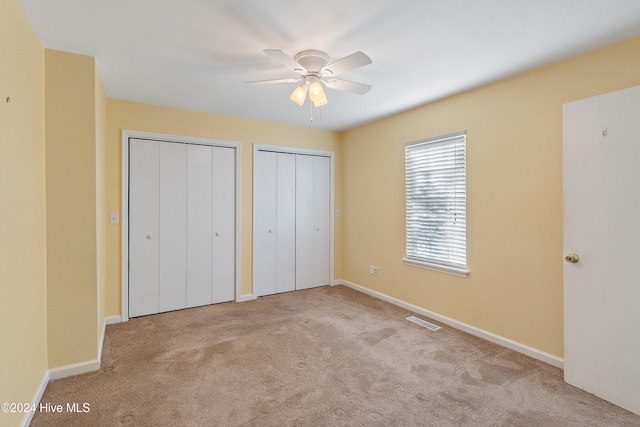 unfurnished bedroom featuring baseboards, visible vents, a ceiling fan, light colored carpet, and two closets