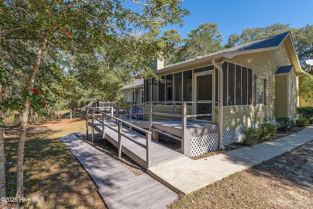 exterior space with a chimney, a wooden deck, and a sunroom