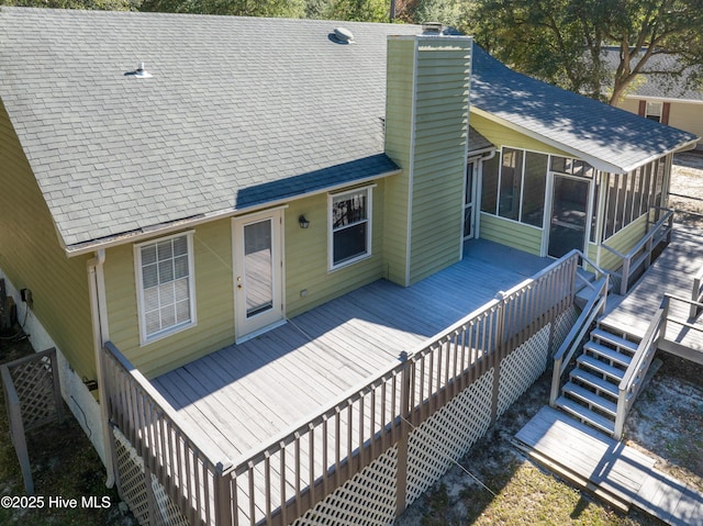 rear view of property with a shingled roof, a sunroom, a chimney, stairway, and a wooden deck