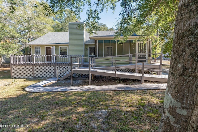 rear view of house featuring a sunroom, a chimney, a lawn, and a wooden deck