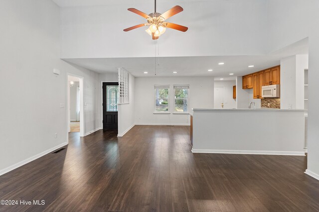 unfurnished living room featuring a towering ceiling, dark wood-type flooring, and ceiling fan