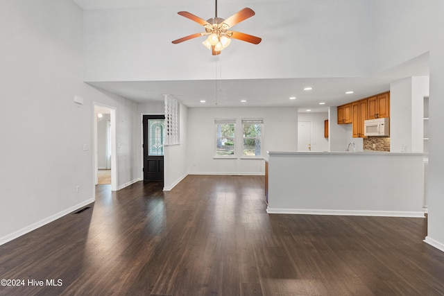 unfurnished living room featuring a ceiling fan, a high ceiling, dark wood finished floors, and baseboards