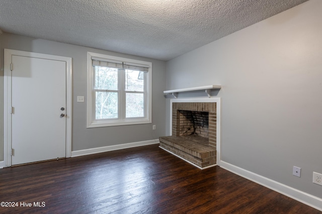 unfurnished living room featuring dark wood-type flooring, a textured ceiling, and a brick fireplace