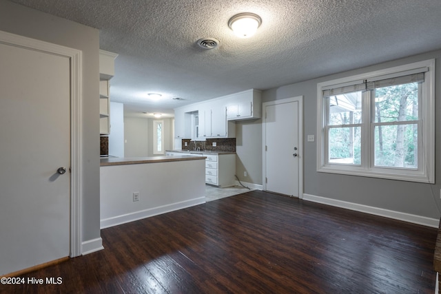 kitchen with kitchen peninsula, dark hardwood / wood-style flooring, tasteful backsplash, a textured ceiling, and white cabinetry