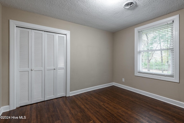 unfurnished bedroom with a textured ceiling, a closet, and dark wood-type flooring