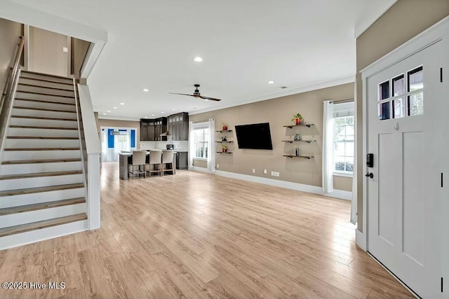 unfurnished living room featuring light wood-type flooring, plenty of natural light, ceiling fan, and ornamental molding