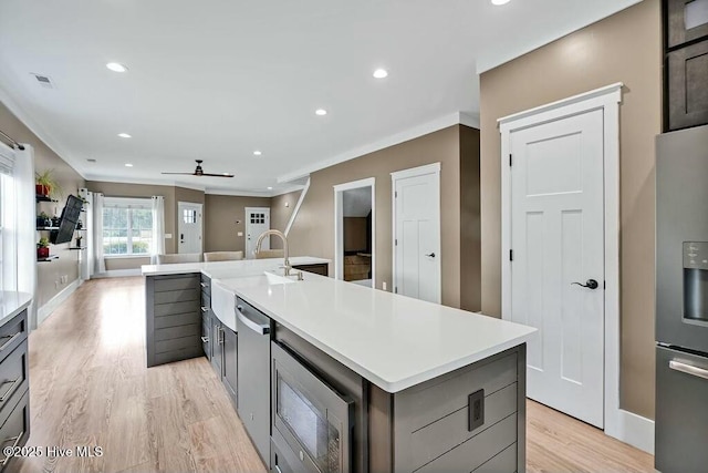 kitchen featuring ceiling fan, stainless steel appliances, light hardwood / wood-style flooring, a kitchen island with sink, and ornamental molding