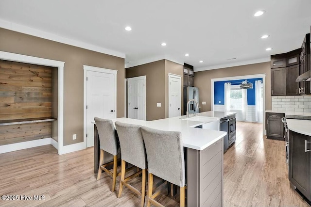 kitchen with light hardwood / wood-style flooring, backsplash, a kitchen island with sink, dark brown cabinets, and appliances with stainless steel finishes