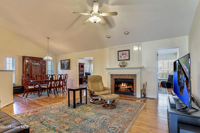 living room with lofted ceiling, a fireplace, ceiling fan, and light wood-type flooring