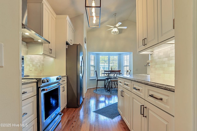 kitchen with lofted ceiling, hanging light fixtures, stainless steel appliances, white cabinets, and wall chimney exhaust hood