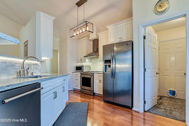 kitchen with sink, wall chimney range hood, white cabinetry, stainless steel appliances, and light stone counters