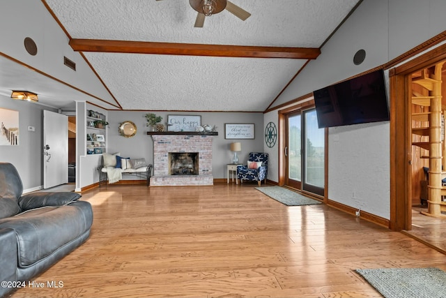 living room with a textured ceiling, light hardwood / wood-style floors, beam ceiling, a fireplace, and ceiling fan