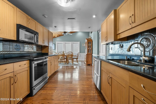 kitchen with light wood-type flooring, appliances with stainless steel finishes, ceiling fan, and backsplash