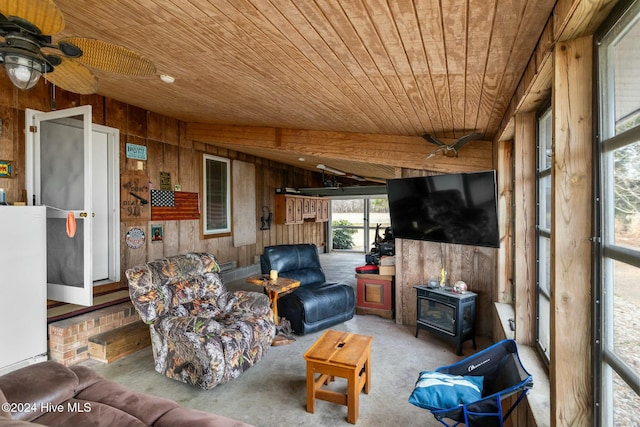 living room featuring ceiling fan, wooden ceiling, wooden walls, and a wood stove