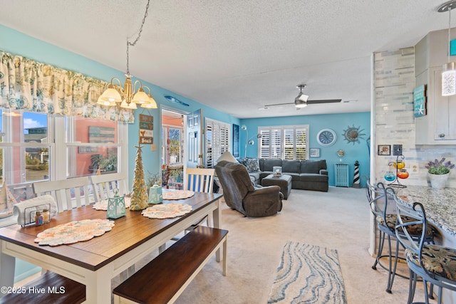 carpeted dining space featuring a textured ceiling and ceiling fan with notable chandelier