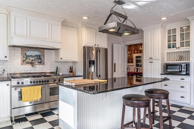 kitchen featuring backsplash, a textured ceiling, a kitchen island, white cabinetry, and stainless steel appliances