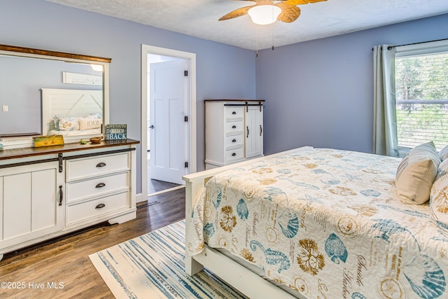 bedroom with ceiling fan, a barn door, a textured ceiling, and dark wood-type flooring