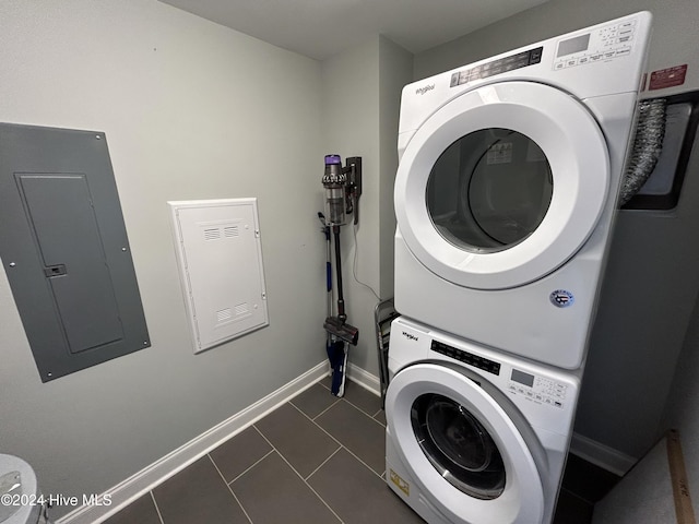 washroom with stacked washer and dryer, electric panel, and dark tile patterned flooring