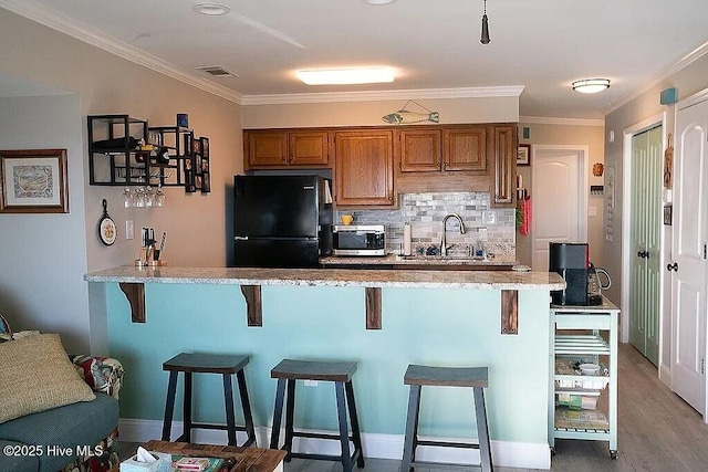 kitchen featuring a kitchen breakfast bar, black refrigerator, sink, crown molding, and tasteful backsplash