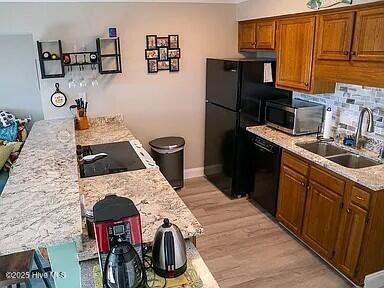 kitchen with backsplash, black appliances, sink, light stone countertops, and light hardwood / wood-style floors