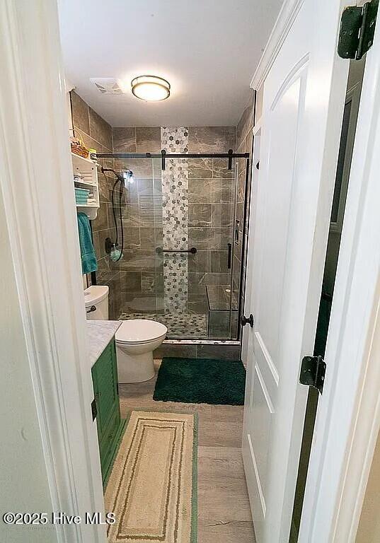 bathroom with hardwood / wood-style floors, vanity, a shower with shower door, and toilet