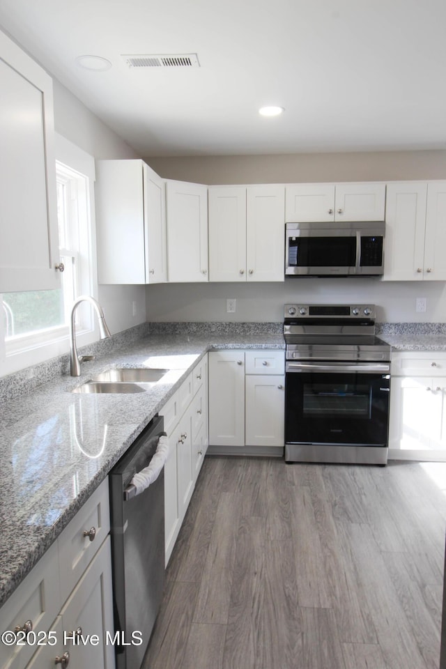 kitchen with appliances with stainless steel finishes, dark hardwood / wood-style flooring, white cabinetry, and sink