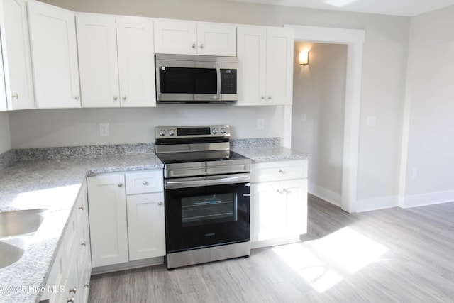 kitchen featuring white cabinets, light stone countertops, stainless steel appliances, and light hardwood / wood-style flooring