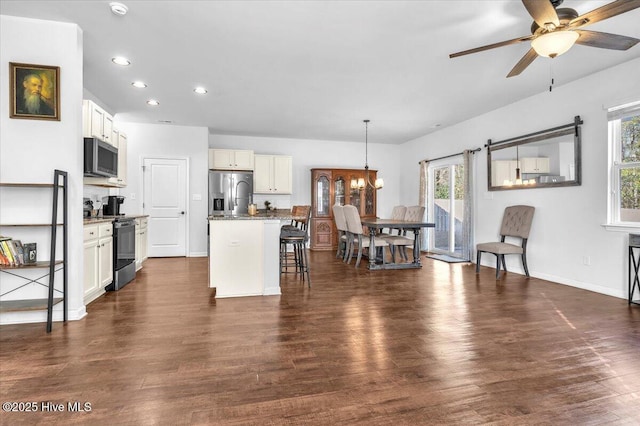 kitchen with dark wood-style floors, a center island with sink, appliances with stainless steel finishes, and a kitchen breakfast bar