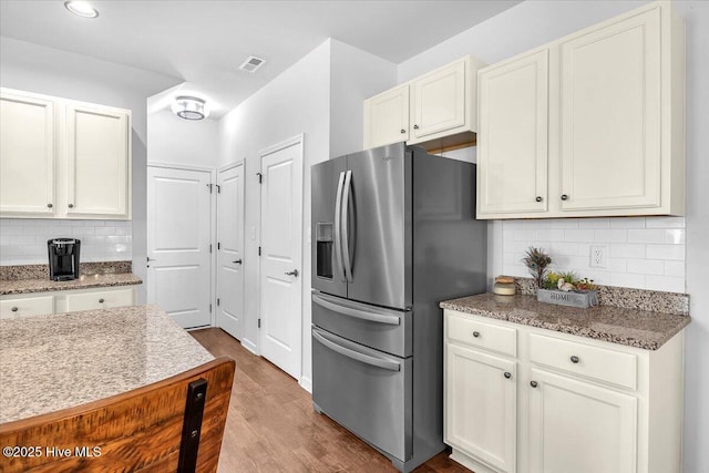 kitchen featuring stone counters, wood finished floors, visible vents, backsplash, and stainless steel fridge with ice dispenser