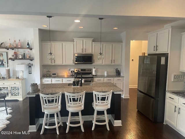 kitchen featuring stainless steel appliances, dark hardwood / wood-style flooring, pendant lighting, a center island with sink, and white cabinets