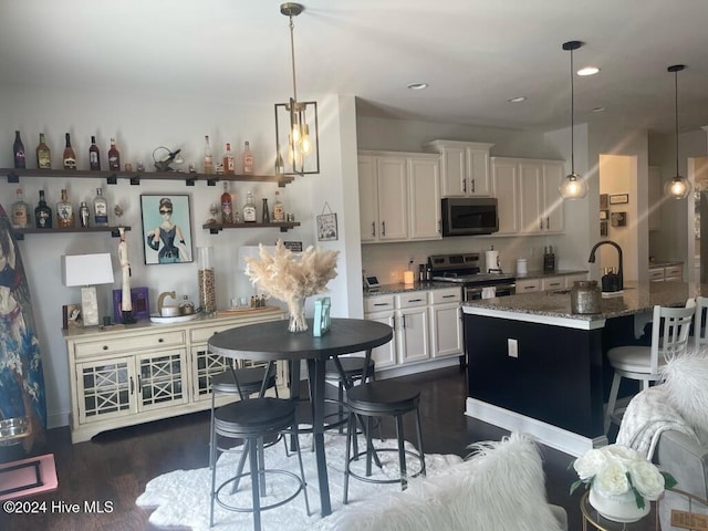 kitchen featuring a center island with sink, a kitchen breakfast bar, dark stone countertops, white cabinetry, and stainless steel appliances