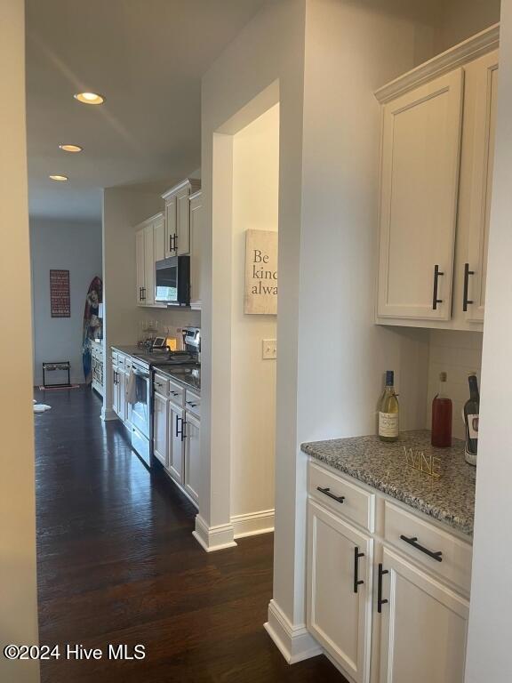 kitchen with electric range, dark hardwood / wood-style floors, tasteful backsplash, light stone counters, and white cabinetry