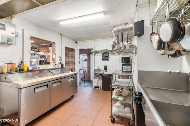 kitchen with stainless steel counters, light tile patterned floors, and brick wall