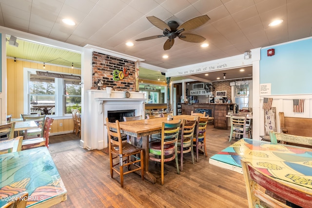 dining space featuring ceiling fan, a fireplace, brick wall, and hardwood / wood-style flooring