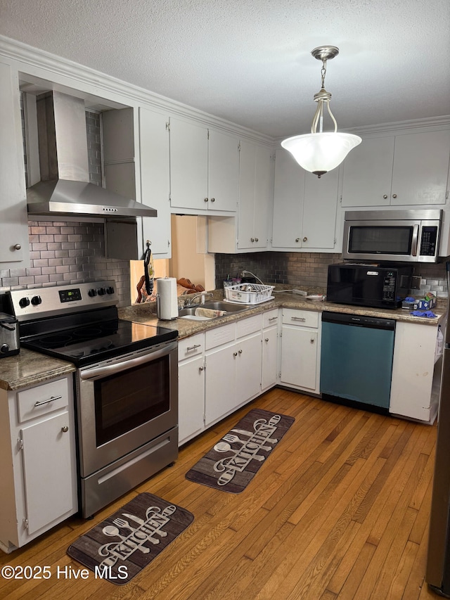 kitchen with pendant lighting, white cabinets, wall chimney exhaust hood, and appliances with stainless steel finishes