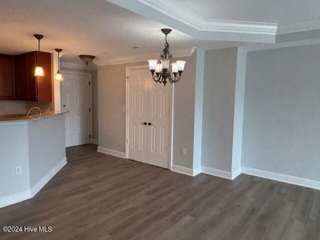 unfurnished dining area with ornamental molding, dark wood-type flooring, and a chandelier