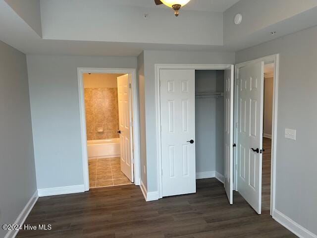 unfurnished bedroom with a raised ceiling, ensuite bath, a closet, and dark wood-type flooring