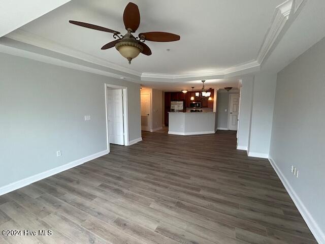 unfurnished living room featuring a tray ceiling, ceiling fan, dark hardwood / wood-style floors, and ornamental molding