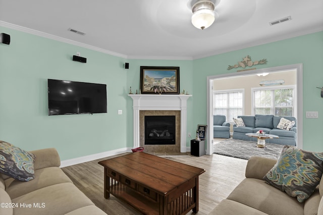 living room with ceiling fan, crown molding, wood-type flooring, and a fireplace