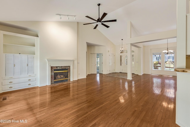 3882 White Blossom Cir, Southport, NC 28461 - unfurnished living room featuring a fireplace, visible vents, high vaulted ceiling, ceiling fan with notable chandelier, and wood finished floors