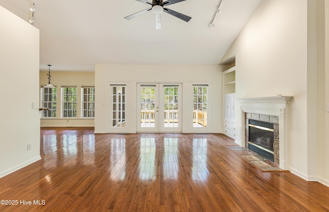 3882 White Blossom Cir, Southport, NC 28461 - unfurnished living room with rail lighting, a ceiling fan, a tiled fireplace, wood-type flooring, and baseboards