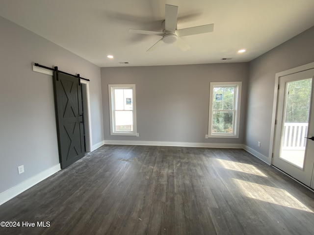 unfurnished room featuring a barn door, ceiling fan, and dark hardwood / wood-style flooring