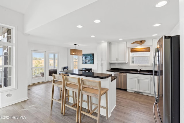 kitchen featuring a kitchen bar, stainless steel appliances, sink, pendant lighting, and white cabinets