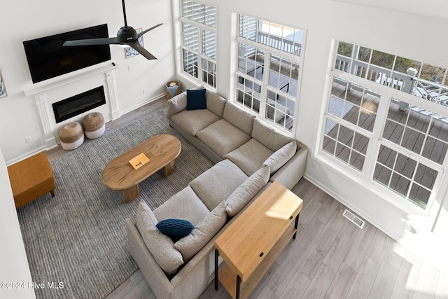 living room with ceiling fan, plenty of natural light, wood-type flooring, and a high ceiling