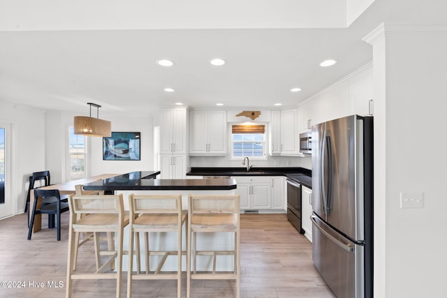 kitchen featuring white cabinets, decorative light fixtures, stainless steel appliances, and a breakfast bar area