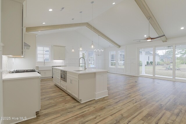 interior space with high vaulted ceiling, ceiling fan with notable chandelier, a stone fireplace, beamed ceiling, and light hardwood / wood-style floors