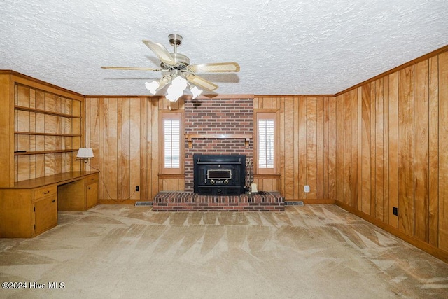 unfurnished living room featuring a wood stove, ceiling fan, wooden walls, a textured ceiling, and light carpet