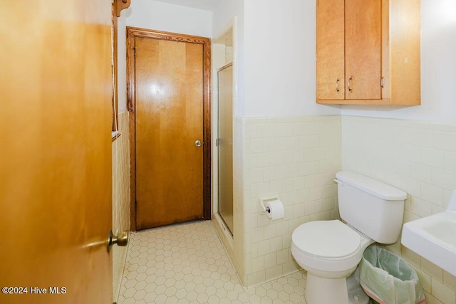 bathroom featuring a shower with door, toilet, and tile walls